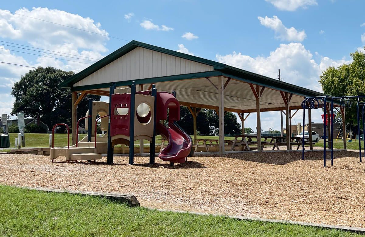 A playground with a slide and swings under a covered pavilion.