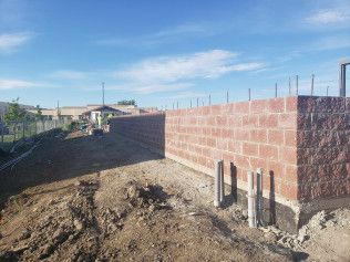 A brick wall is being built in a dirt field.