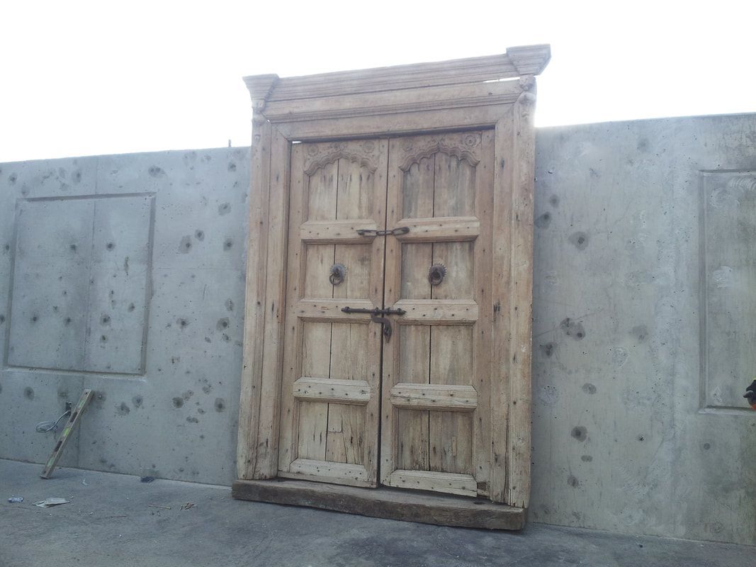 A large wooden door is sitting in front of a concrete wall.