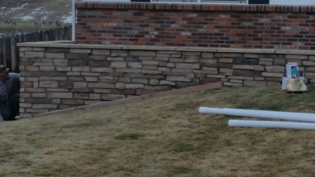 A brick wall is surrounded by grass and pipes in front of a house.
