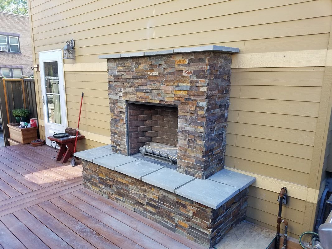 A stone fireplace is sitting on a wooden deck in front of a house.
