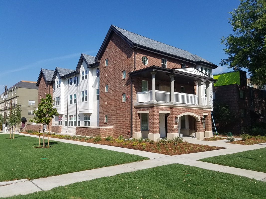 A large brick building with a porch and a sidewalk in front of it.