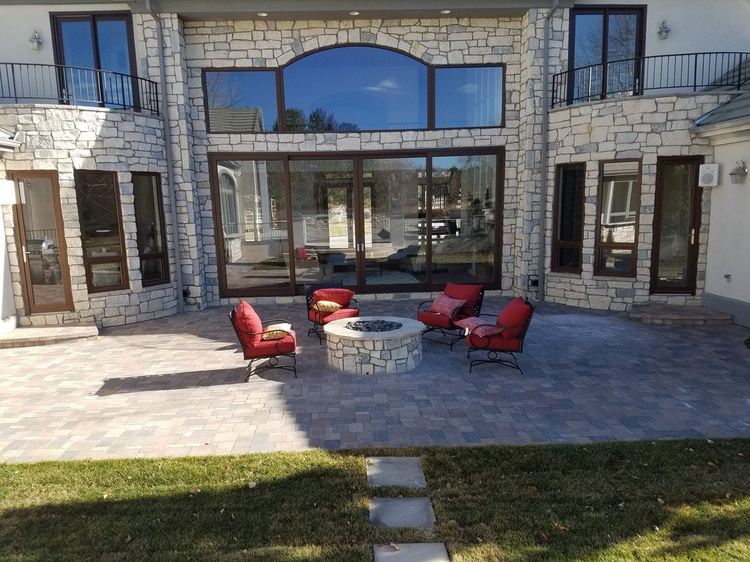 A patio with a fire pit and chairs in front of a large house.
