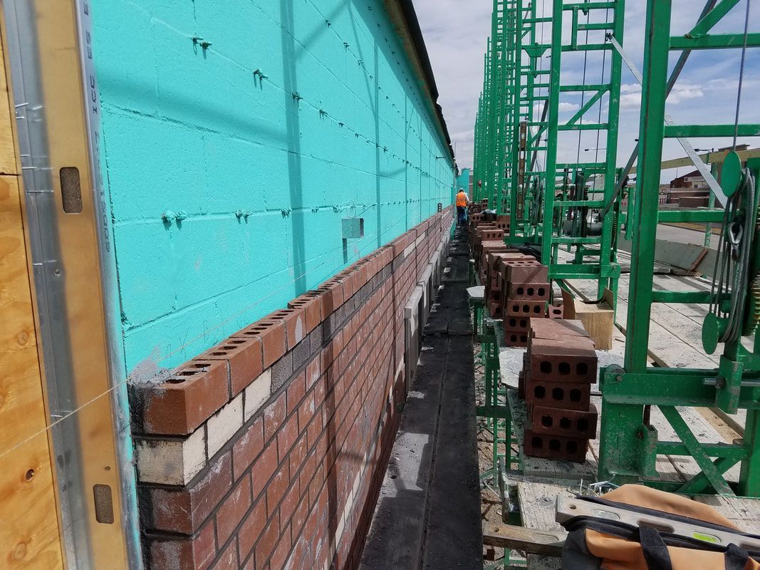 A brick wall is being built with a green crane in the background.