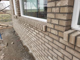 A brick wall with a window on it is being built.