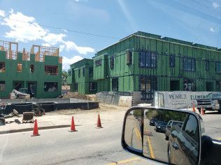 A car is driving down a street in front of a building under construction.