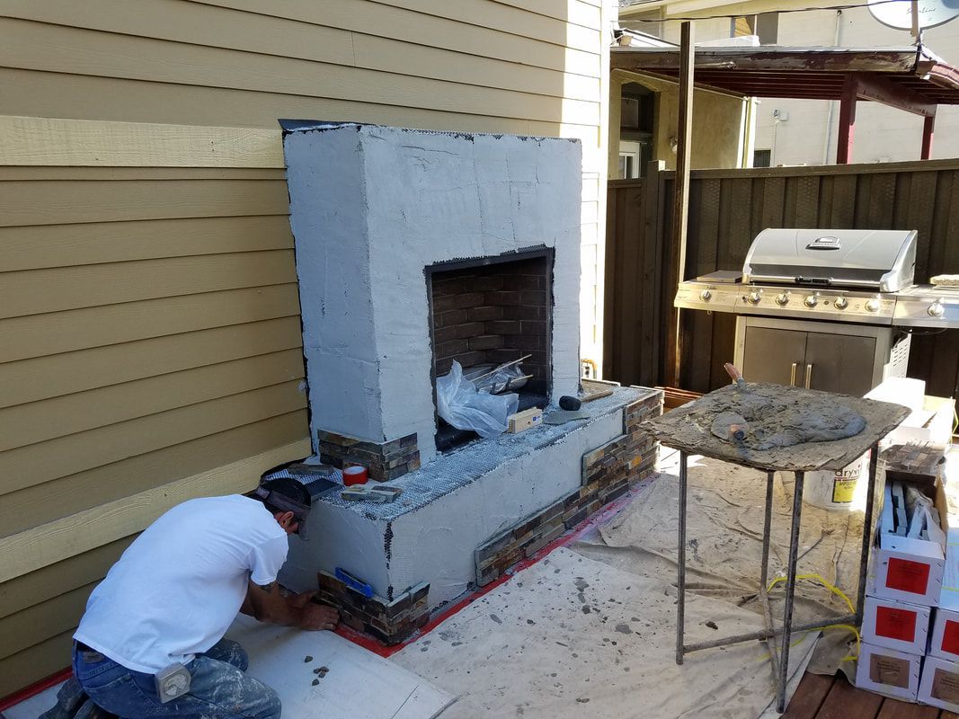 A man is working on a fireplace outside of a house