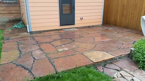 A dog house is sitting on top of a stone patio next to a wooden fence.