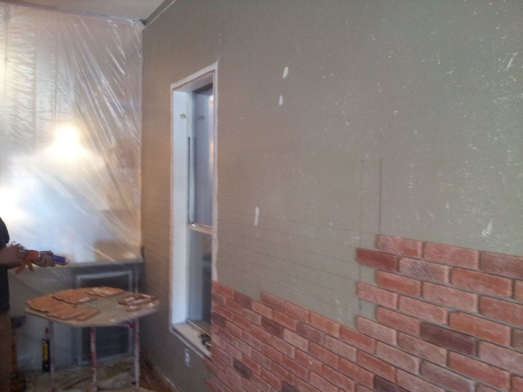 A man is working on a brick wall in a room.