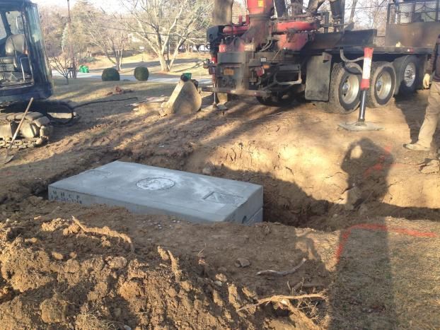 Construction site. Concrete box lowered into a hole with a crane. Dirt surrounds the excavation.