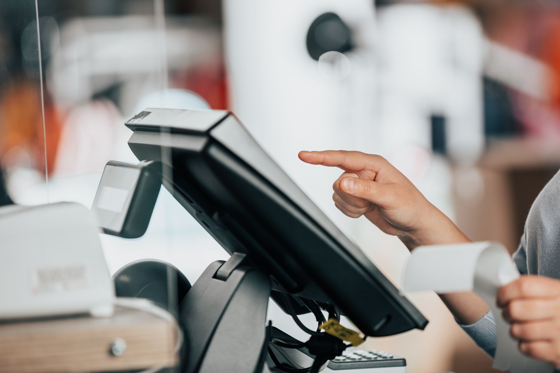 Customer taps a retail touchscreen checkout terminal while holding a card reader in a store.