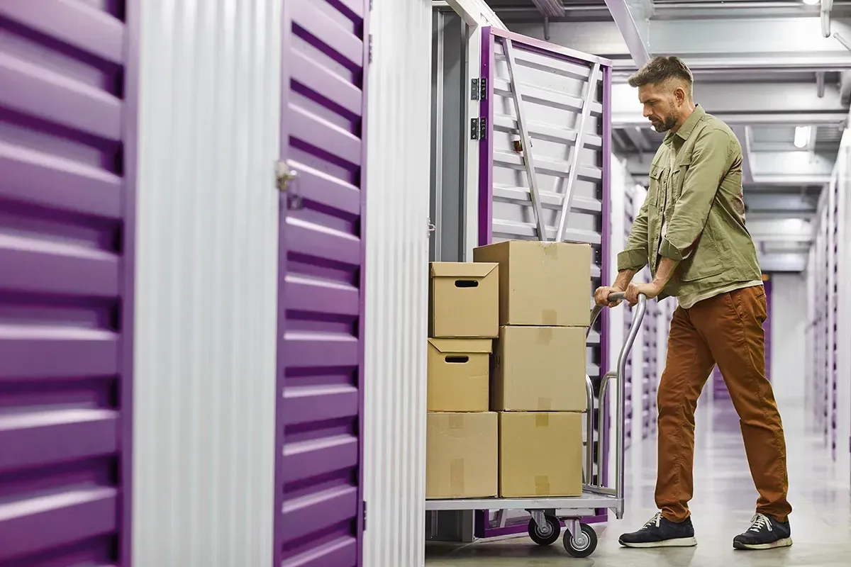 Man loading boxes onto a cart in a purple storage unit hallway.