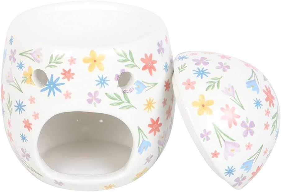 Een keramische oliebrander met bloemenmotief staat naast een klein flesje kaneelolie op een houten ondergrond.