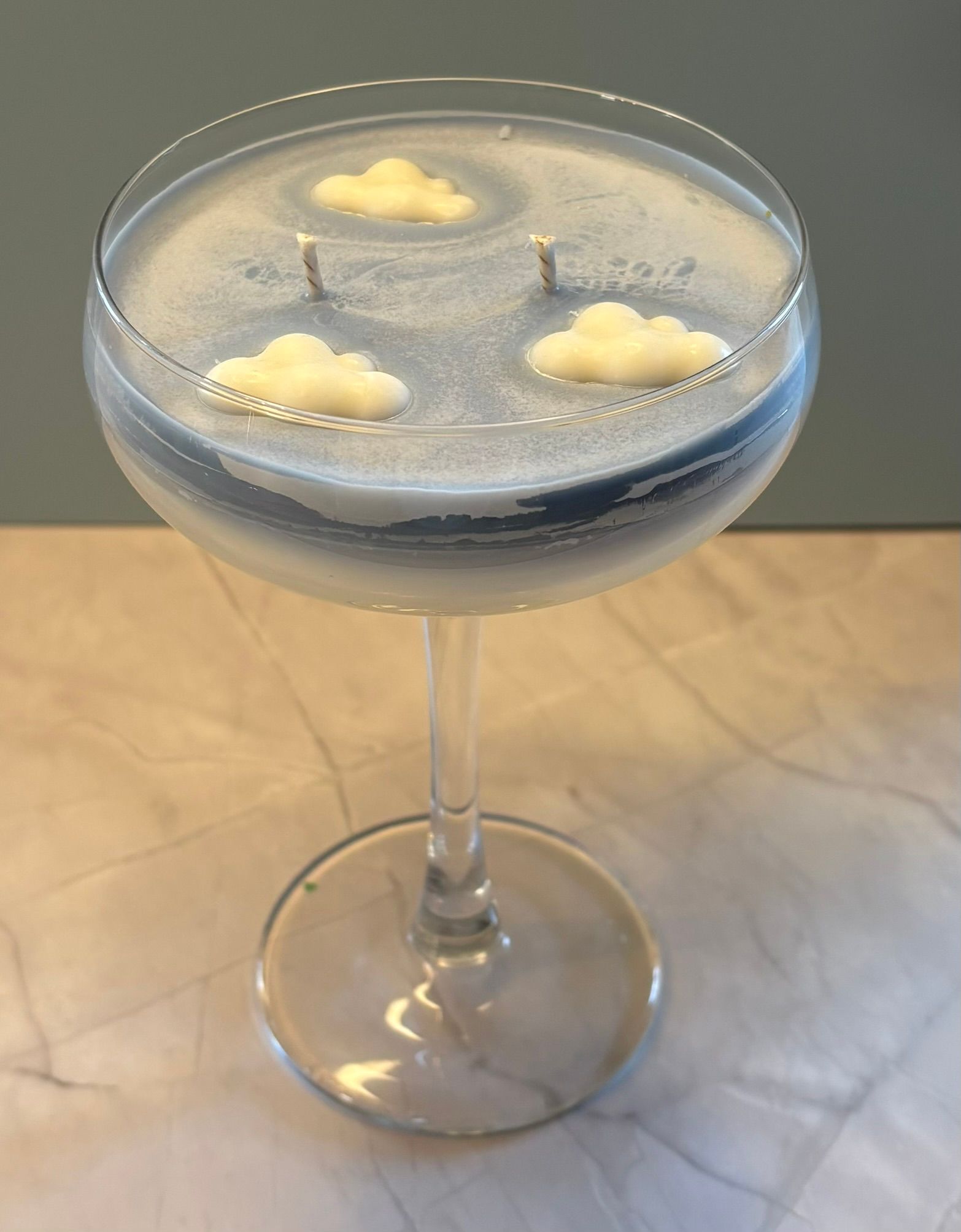 Een blauwe kaars met een hemelmotief in een glazen voetje, voorzien van twee lonten en drie kleine, witte decoratieve wolkjes van was.