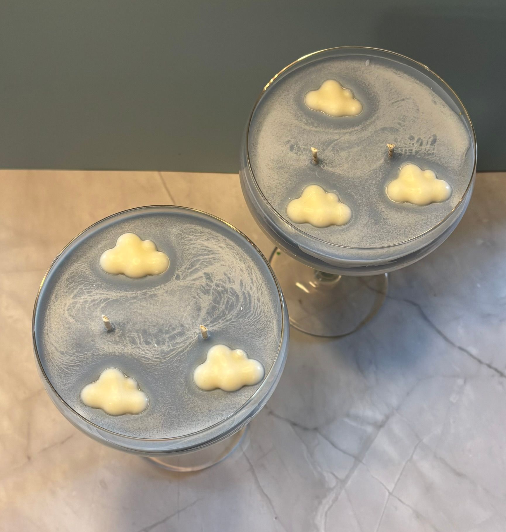 Een blauwe kaars met een hemelmotief in een glazen voetje, voorzien van twee lonten en drie kleine, witte decoratieve wolkjes van was.