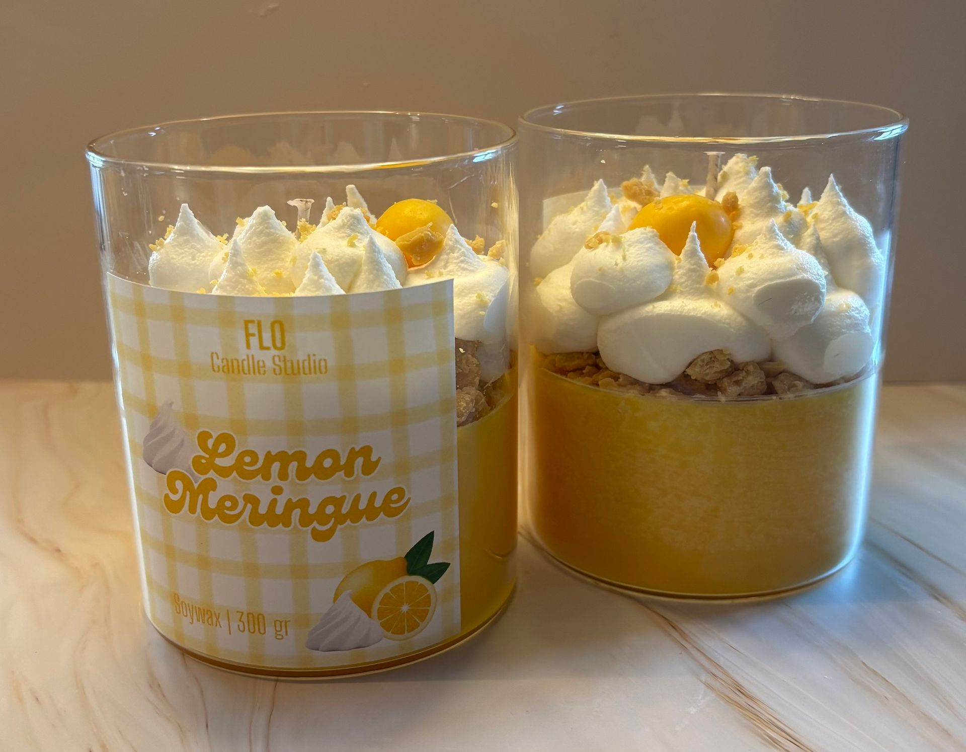 Twee glazen kaarsen versierd als citroenmeringuetaarten, met gele was, kruimelstructuren en met spuitzak aangebrachte witte was in de vorm van 