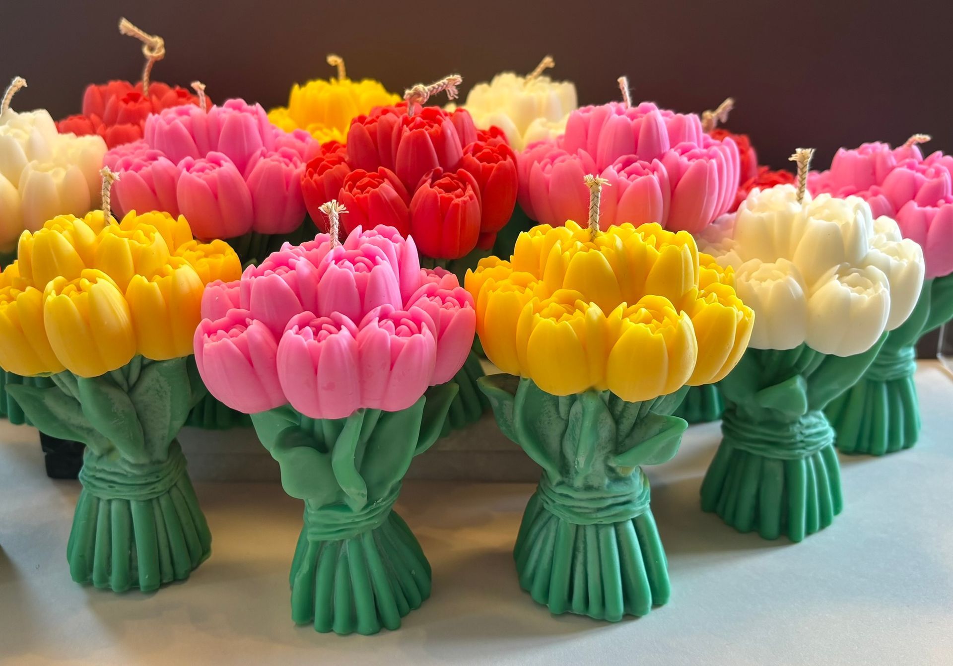 Een groepje kaarsen in de vorm van een tulpenboeket, in verschillende kleuren zoals geel, roze, rood en wit, is op een oppervlak gerangschikt.