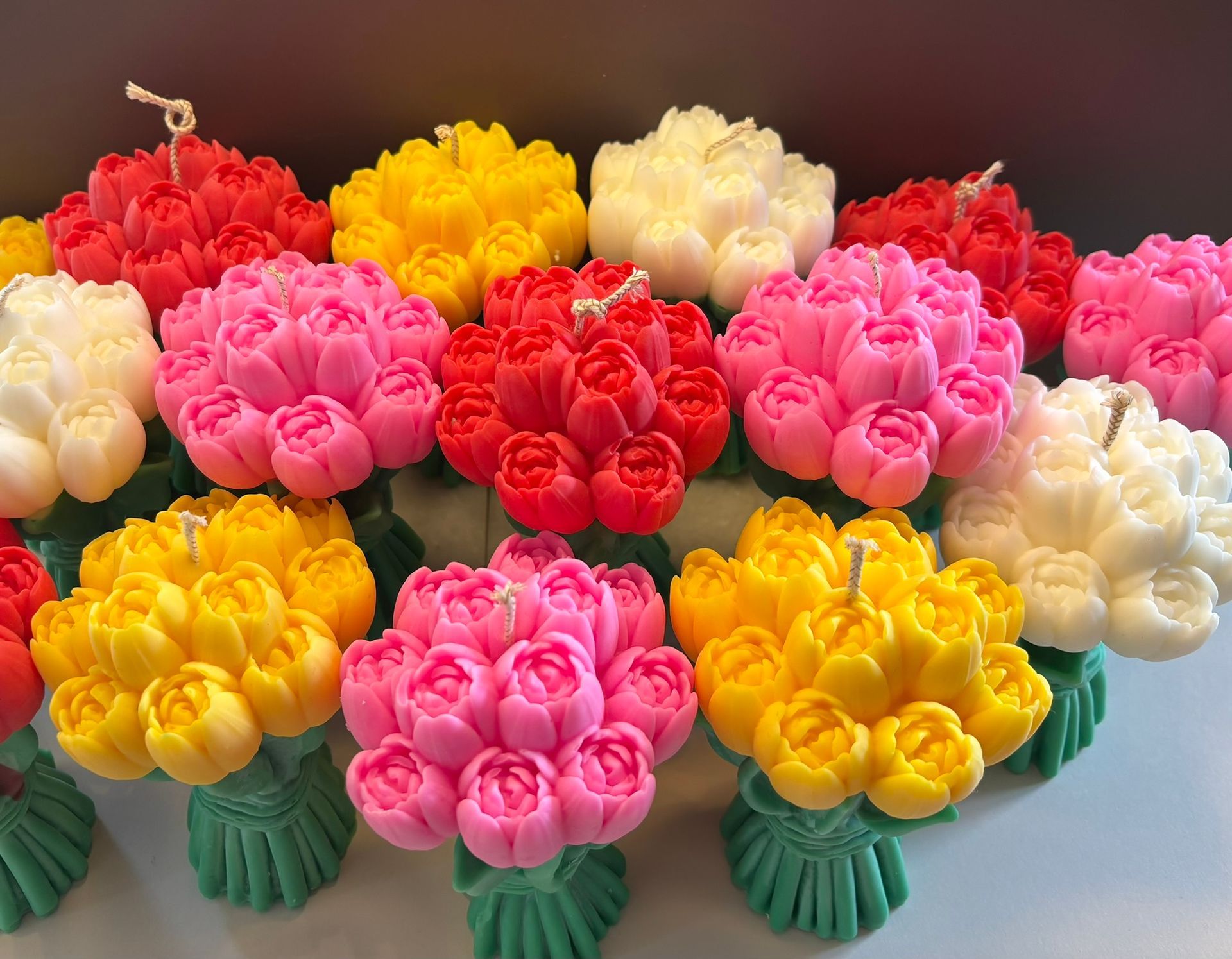 Diverse kaarsenarrangementen in de vorm van kleine, kleurrijke boeketten tulpen in tinten rood, roze, geel en wit.