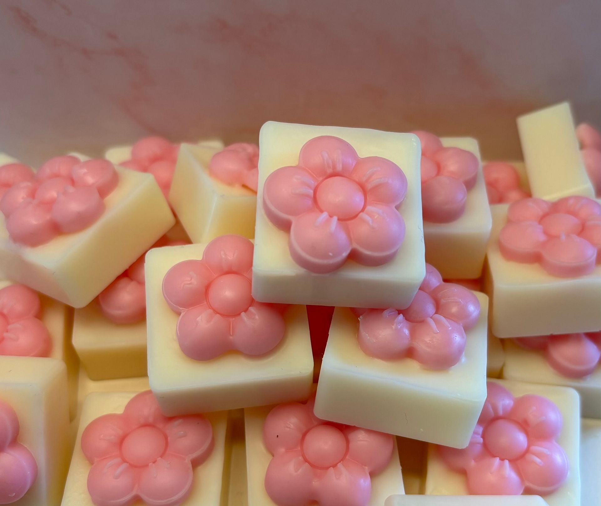 Een stapel vierkante, crèmekleurige geurblokjes, elk met daarop een klein, roze bloempje met vijf blaadjes.