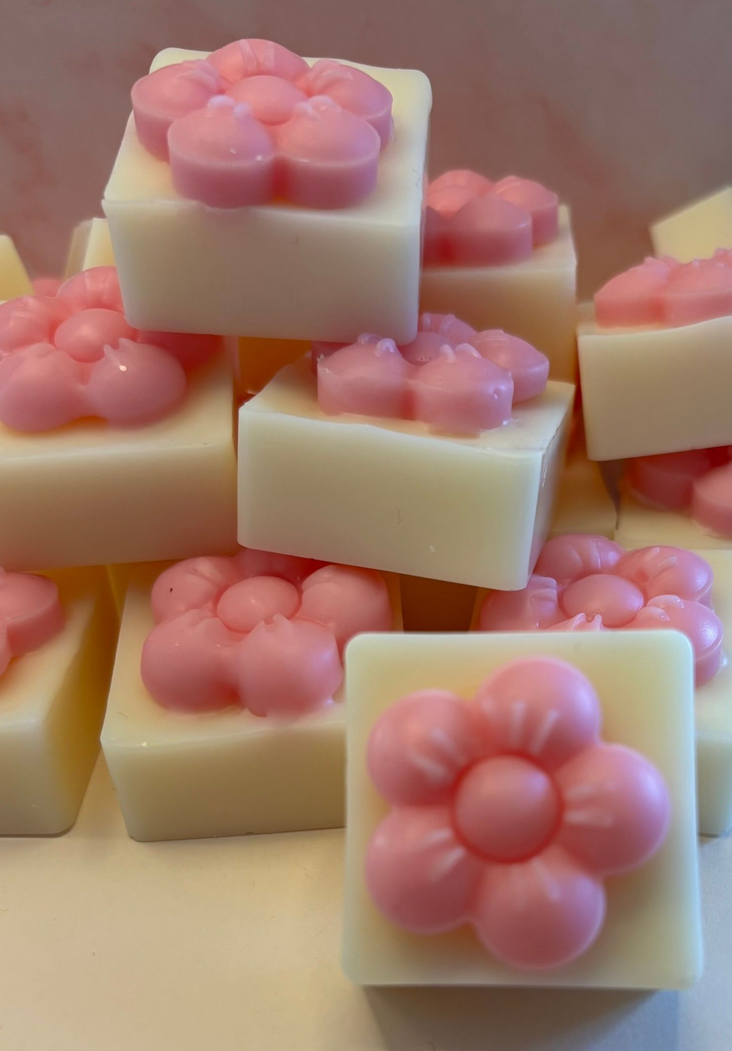 Een stapel vierkante, crèmekleurige geurblokjes, elk met daarop een klein, roze bloempje met vijf blaadjes.