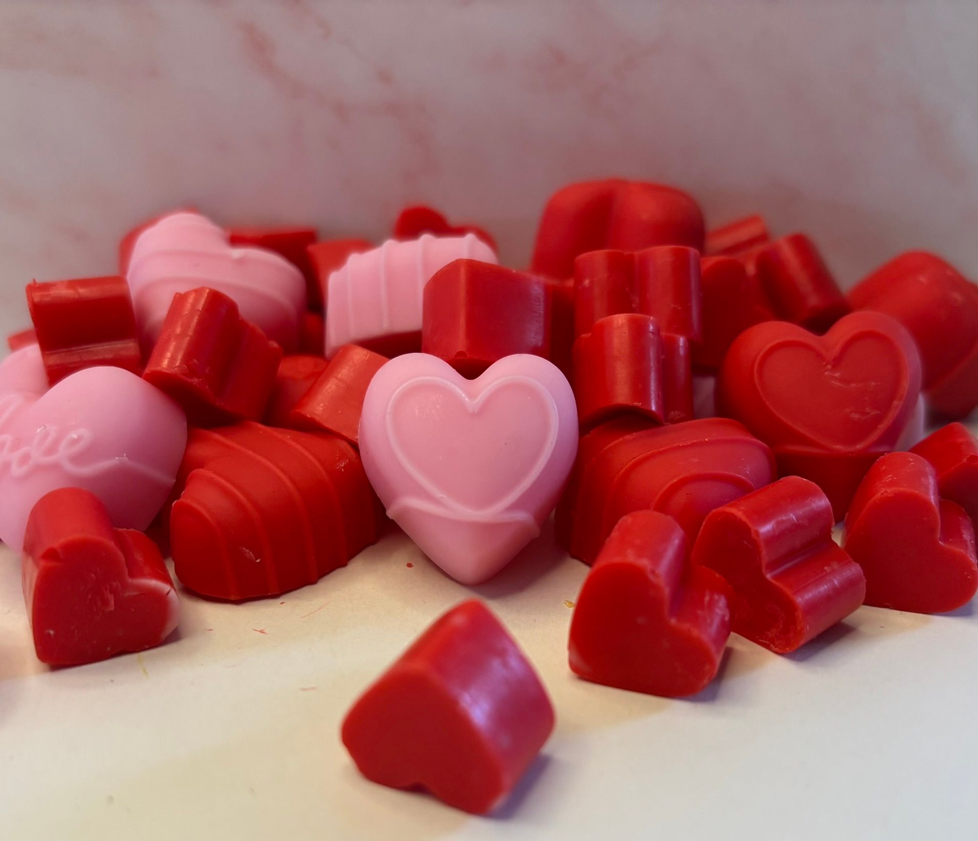 Een verspreide hoop rode en lichtroze hartvormige was smelt op een witte ondergrond tegen een gemarmerde achtergrond.