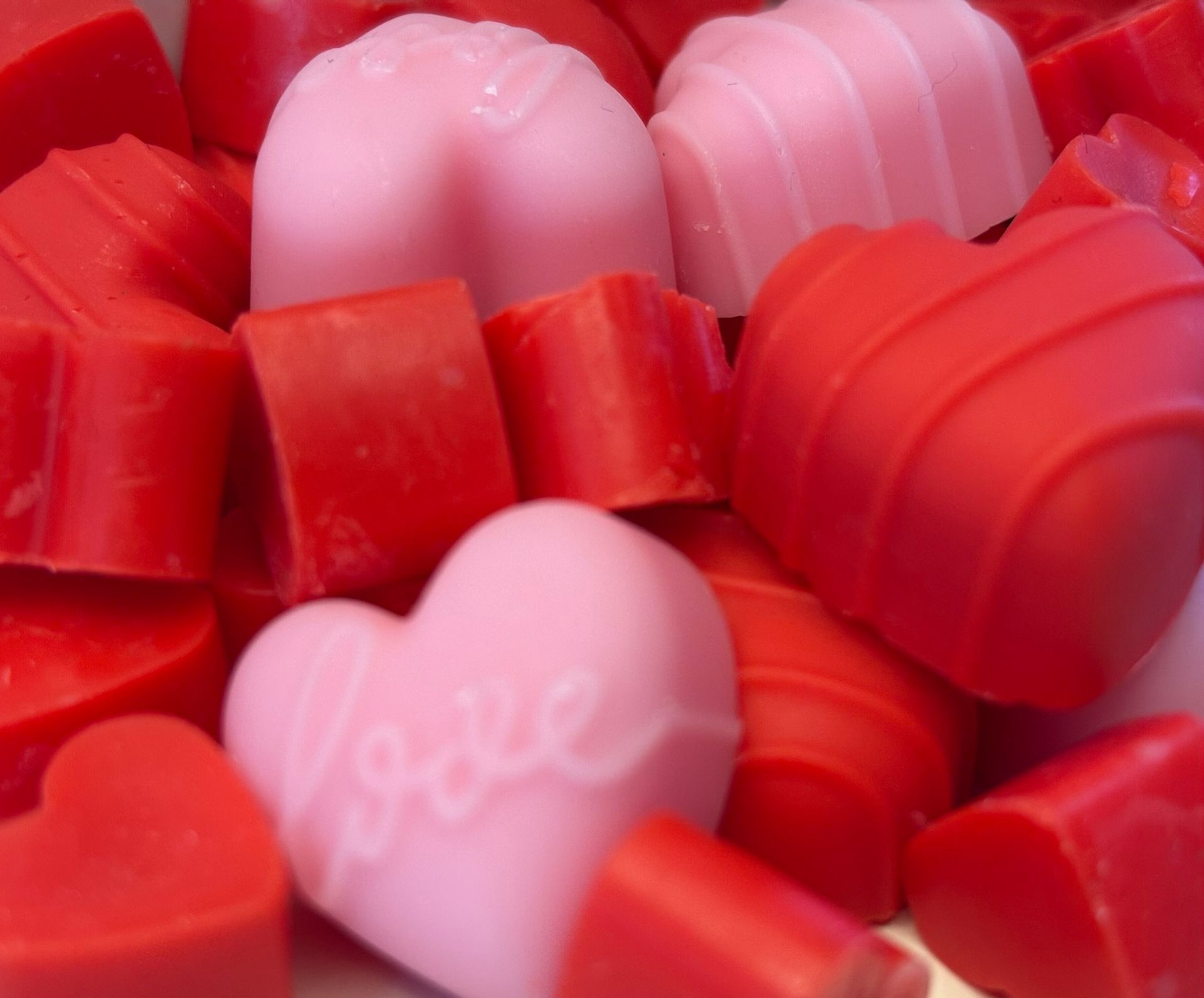Een verspreide hoop rode en lichtroze hartvormige was smelt op een witte ondergrond tegen een gemarmerde achtergrond.