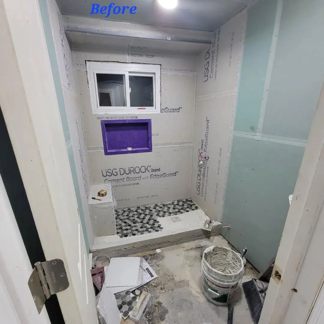 Bathroom renovation in progress: gray walls, small window, purple niche, unfinished floor with debris.