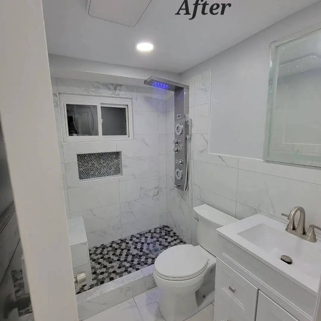 Newly renovated white bathroom with marble tile, shower and toilet.