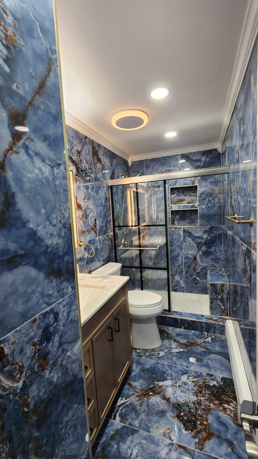 Blue marble bathroom with gold fixtures and glass shower.
