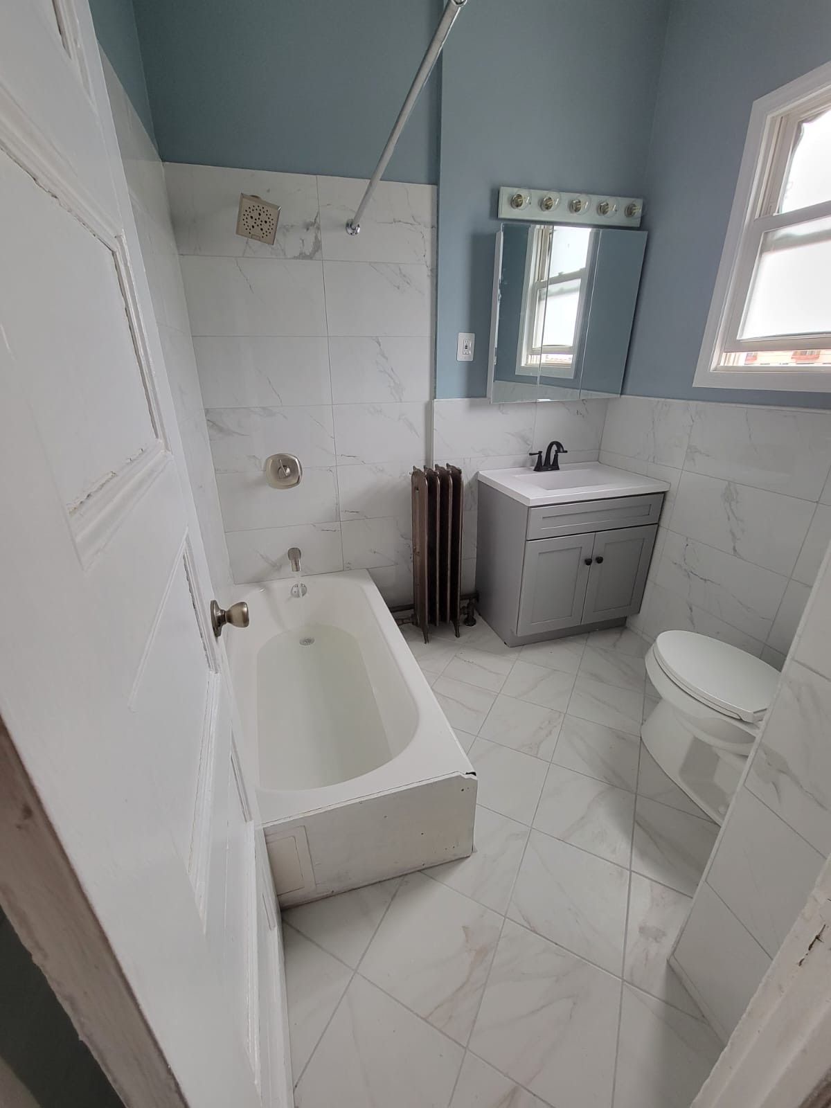 White tiled bathroom with bathtub, sink, and toilet; light blue walls.
