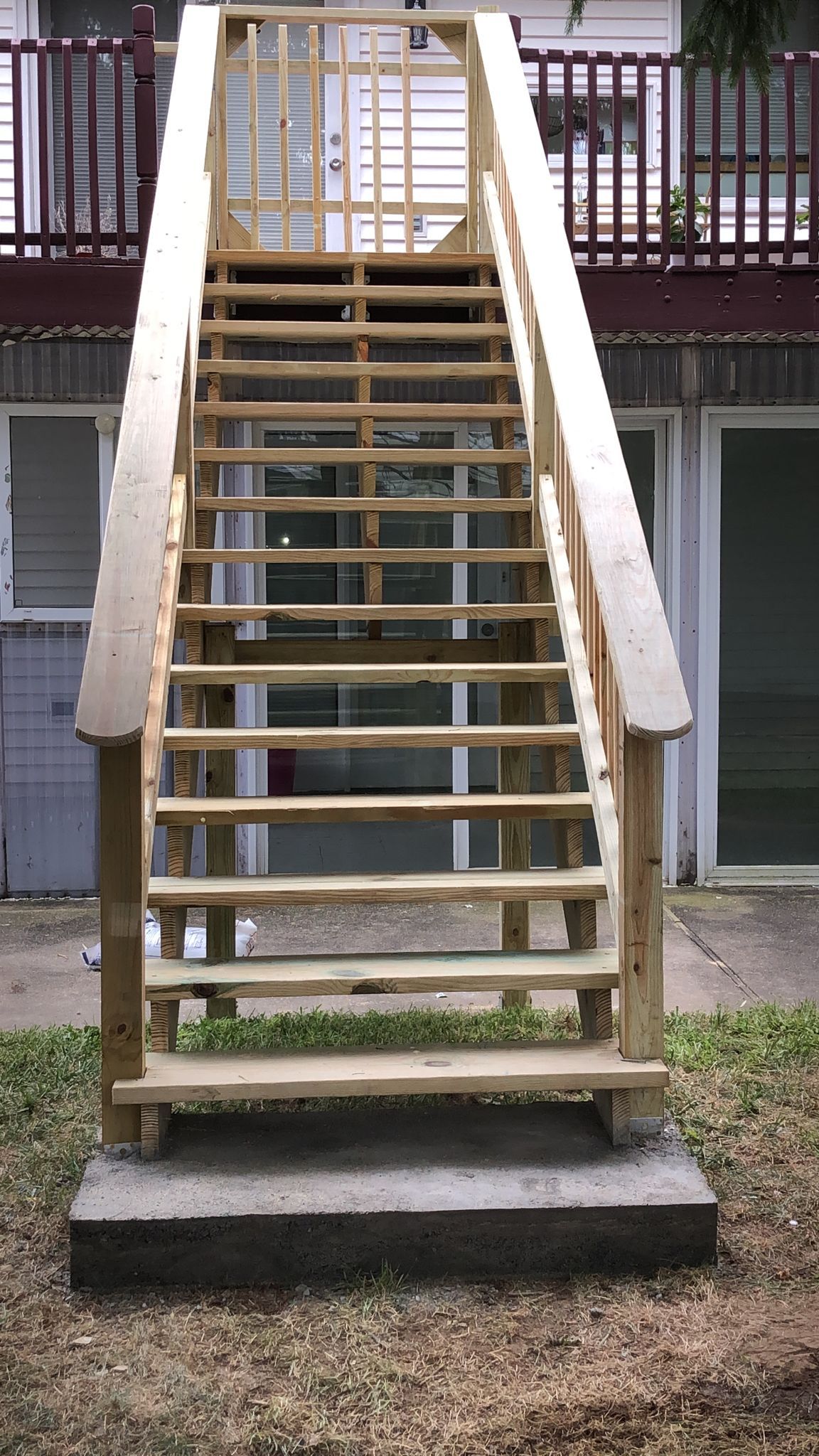 Wooden outdoor staircase leading up to a building entrance, situated on a concrete base.