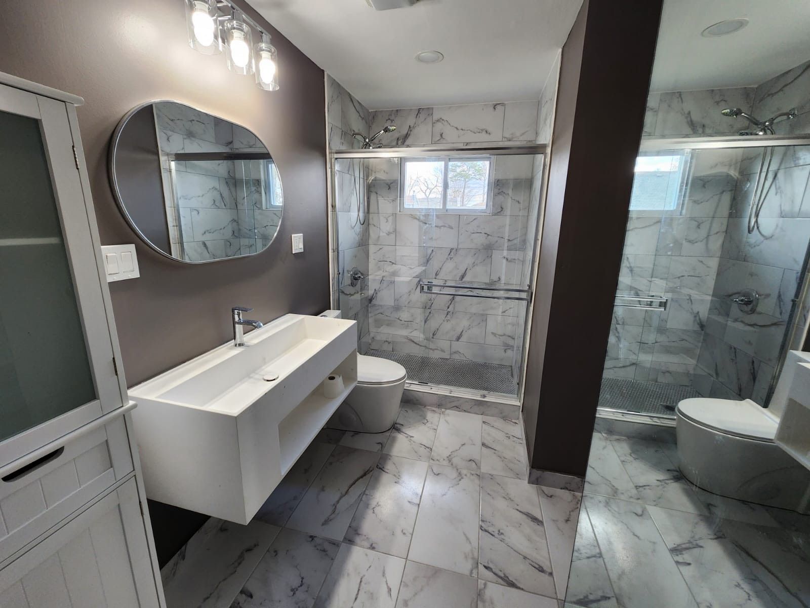 Modern bathroom with white marble tile, floating white vanity, and glass shower.