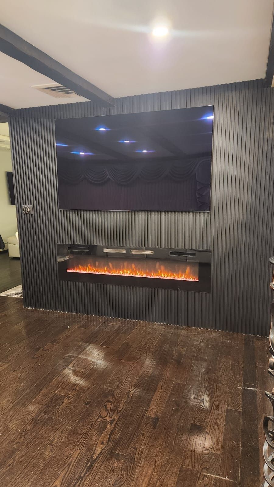 Black media wall with electric fireplace and TV, installed on wood floor.