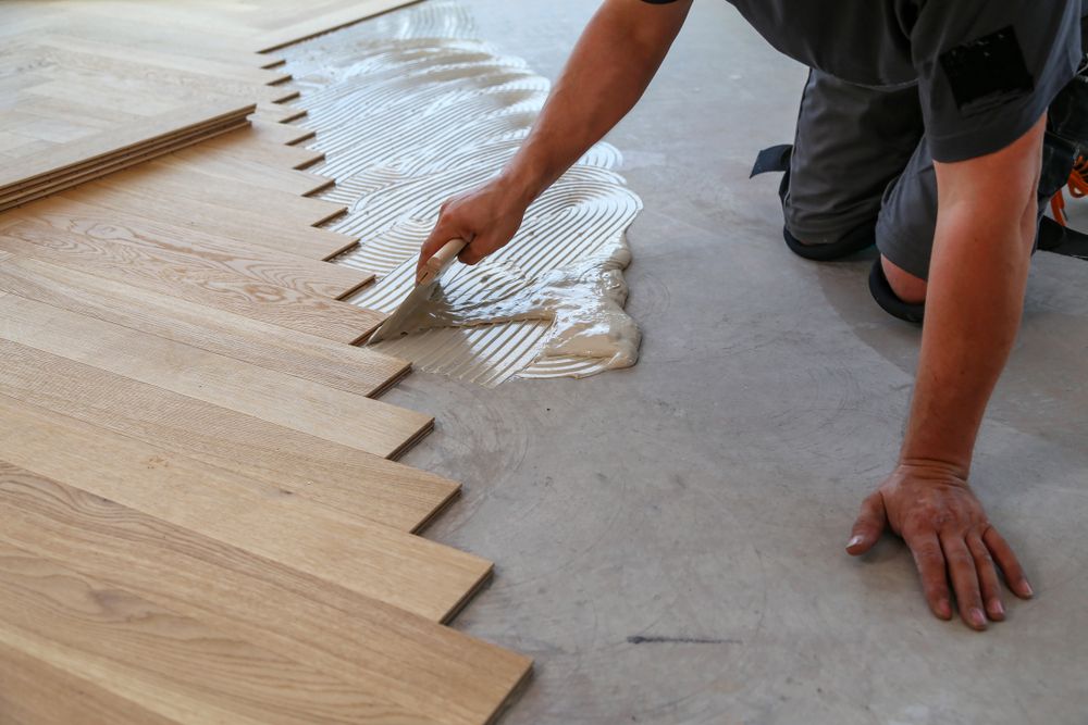 A Man is Applying Adhesive to a Wooden Floor — Taggerts Discount Carpets & Vinyls In California Gully, VIC