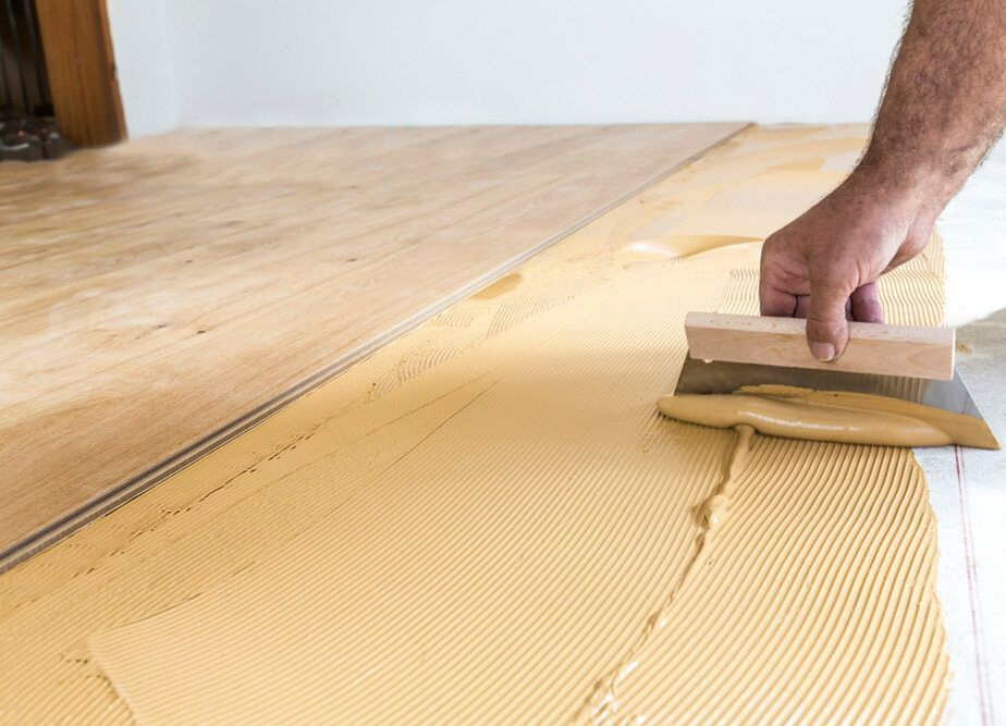 A Person is Applying Adhesive to a Wooden Floor With a Spatula — Taggerts Discount Carpets & Vinyls In California Gully, VIC