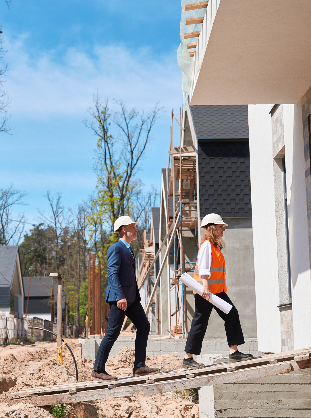 A man and a woman are walking in front of a building under construction.
