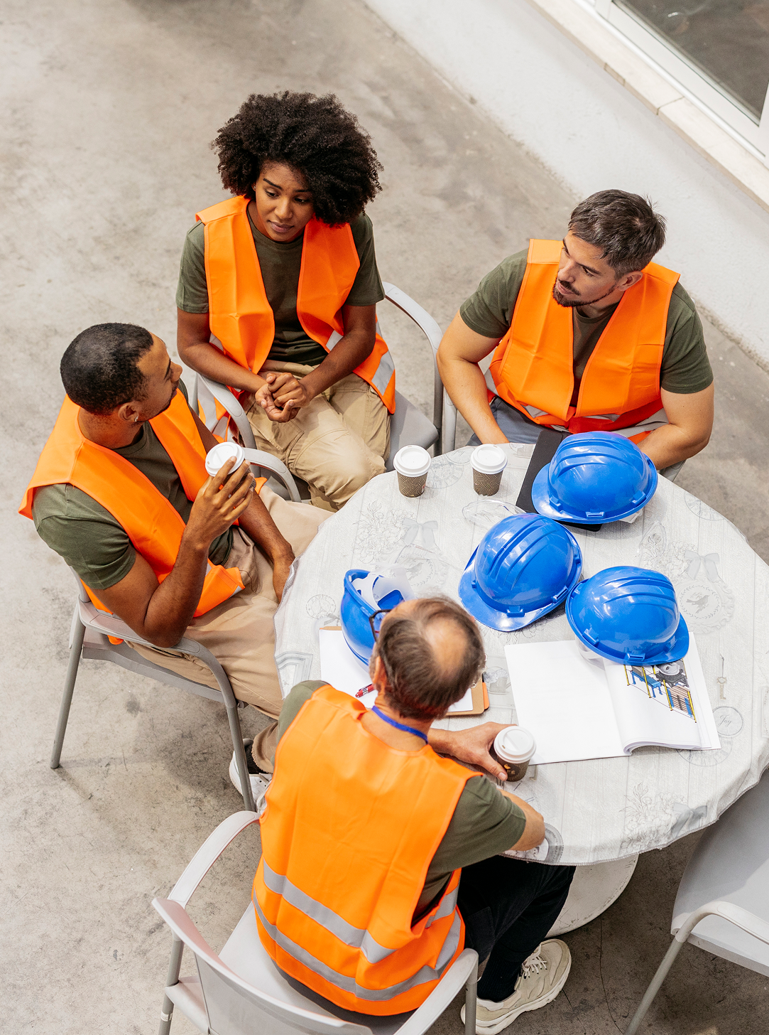 A group of construction workers are sitting around a table with hard hats.