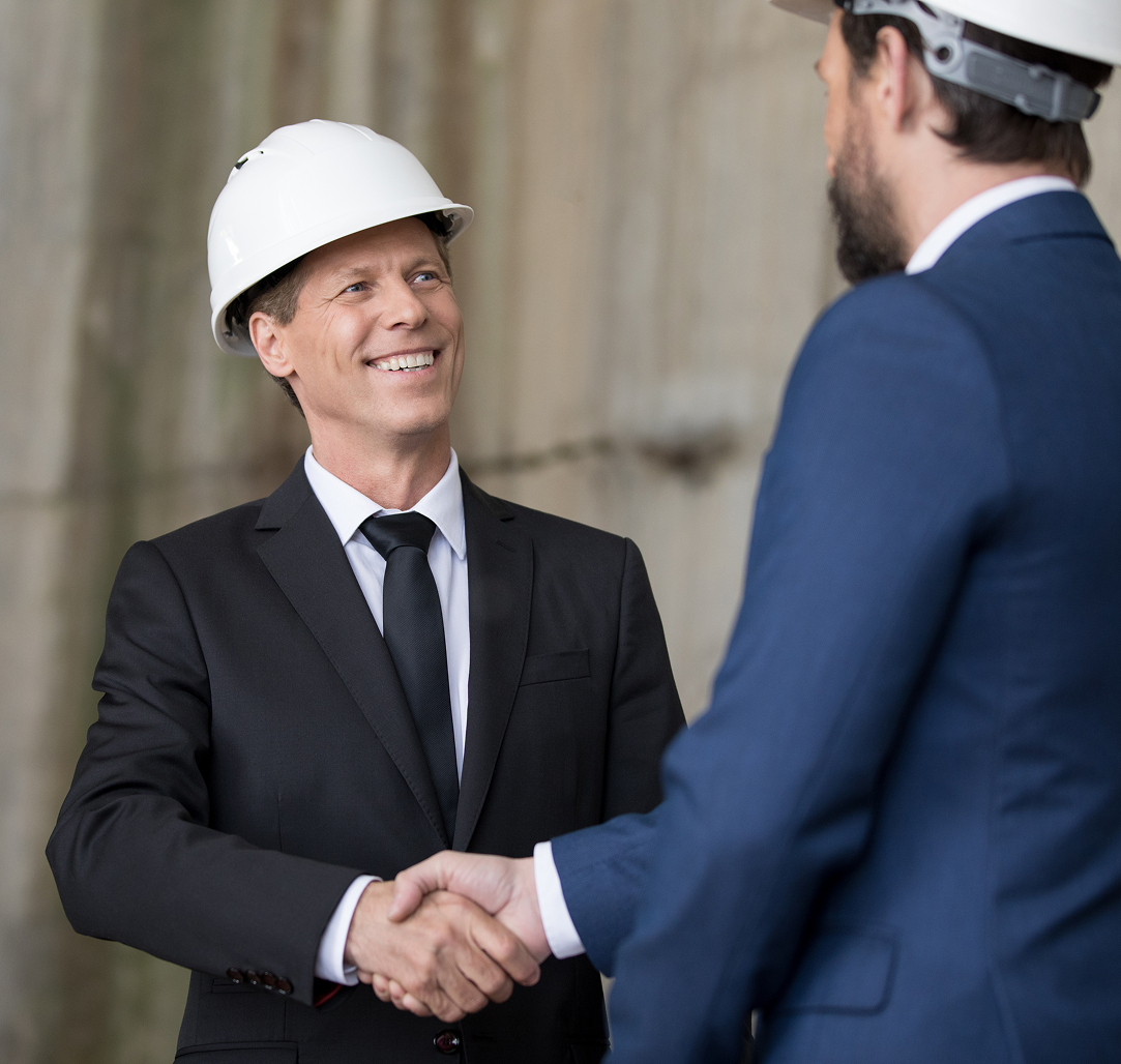 A man wearing a hard hat is shaking hands with another man in a suit.