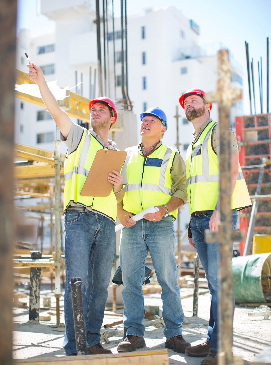 A group of construction workers are standing on a construction site looking up at something.