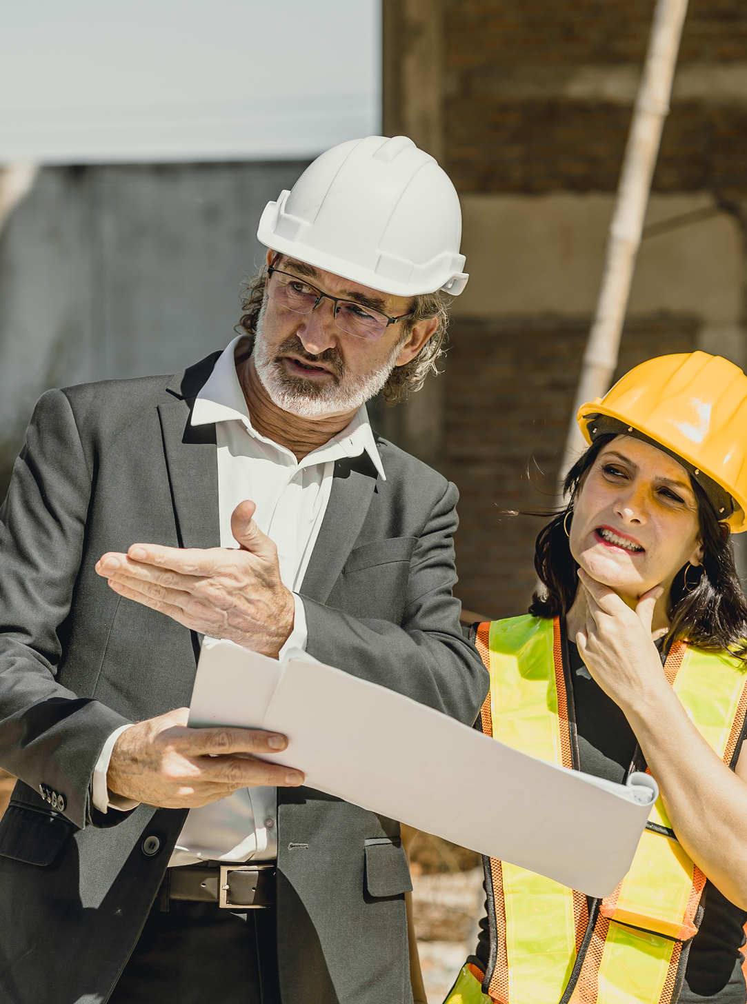 A man and a woman wearing hard hats are looking at a piece of paper.