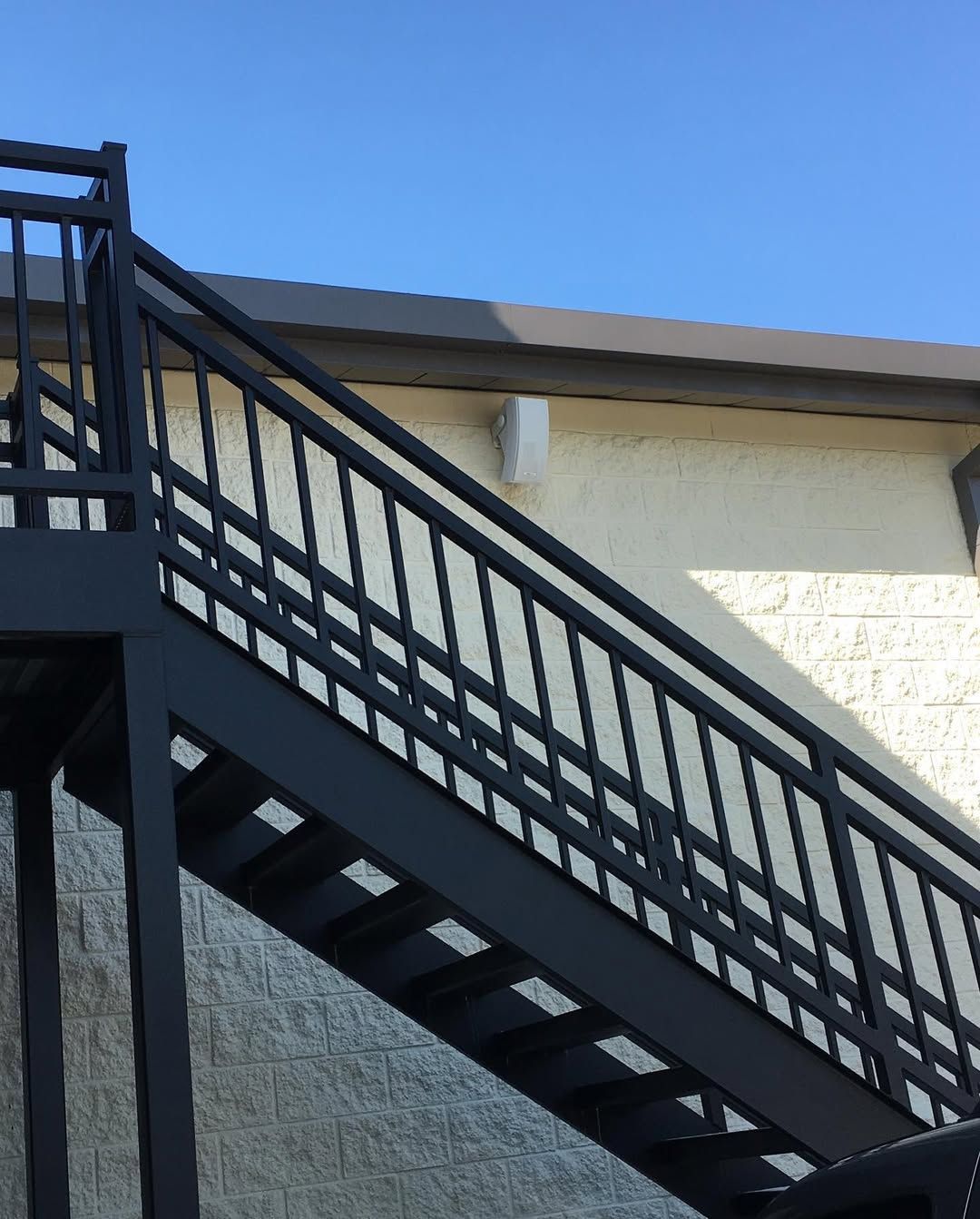 Black metal exterior staircase against a light tan building and a blue sky.