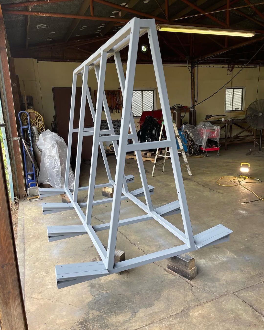 A-frame metal structure painted gray, resting on wooden blocks in a workshop.