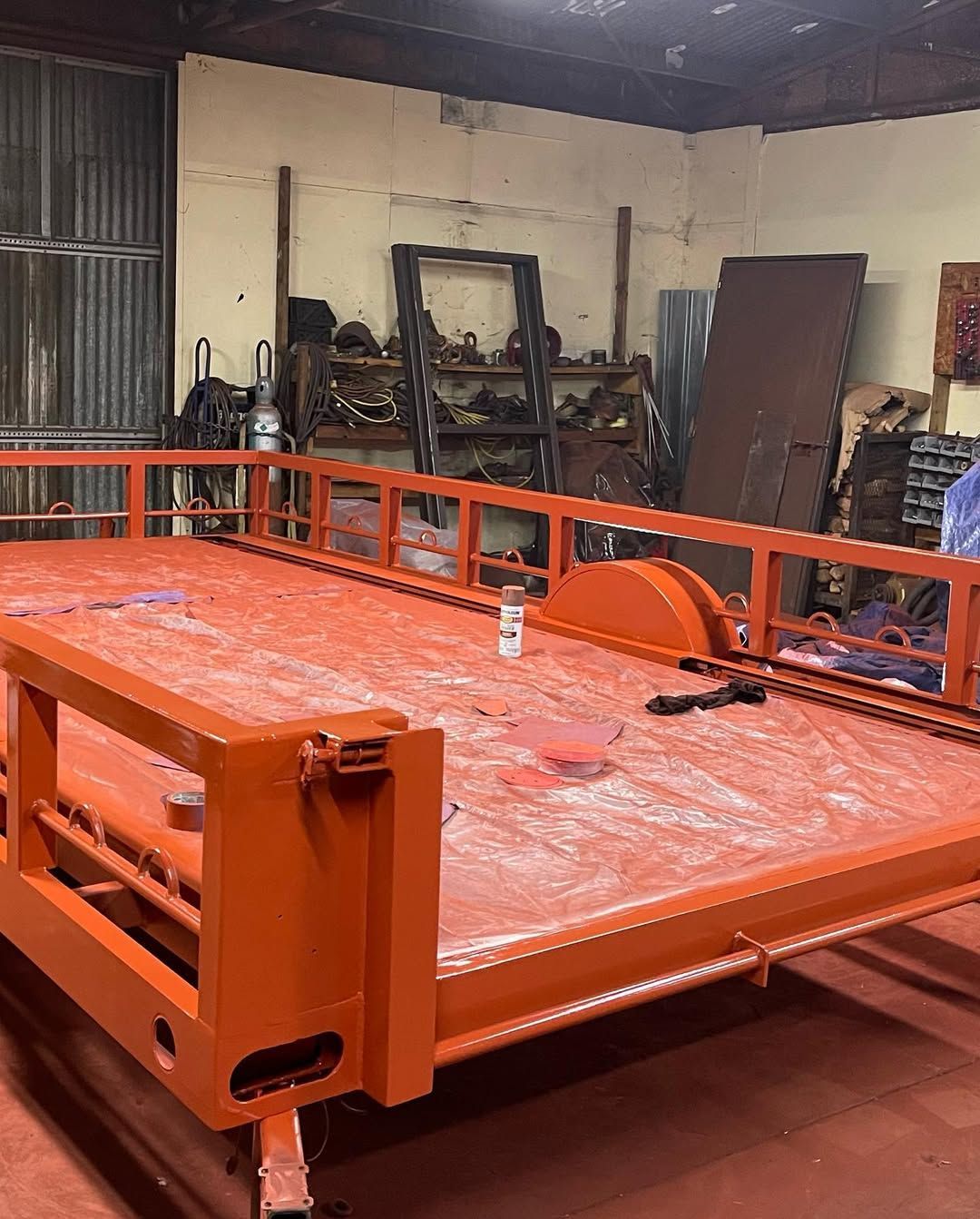 Orange flatbed trailer in a workshop, partially painted.
