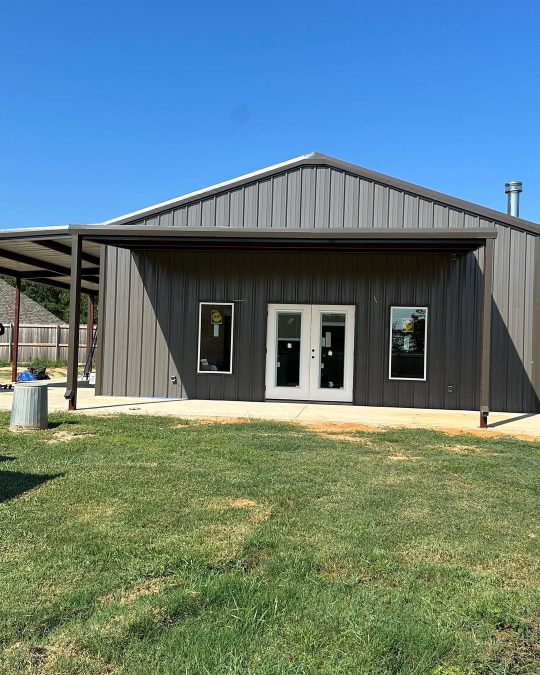 A gray metal building with a brown awning and white double doors, windows on either side.