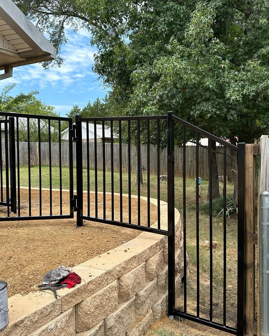 Black metal fence with gate, set on a stone retaining wall, with a backyard view.