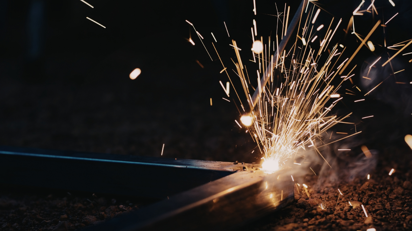 Welding sparks fly from metal against a dark background.