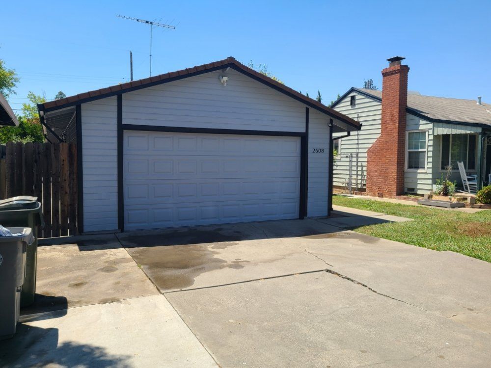 A white garage with a brick house in the background