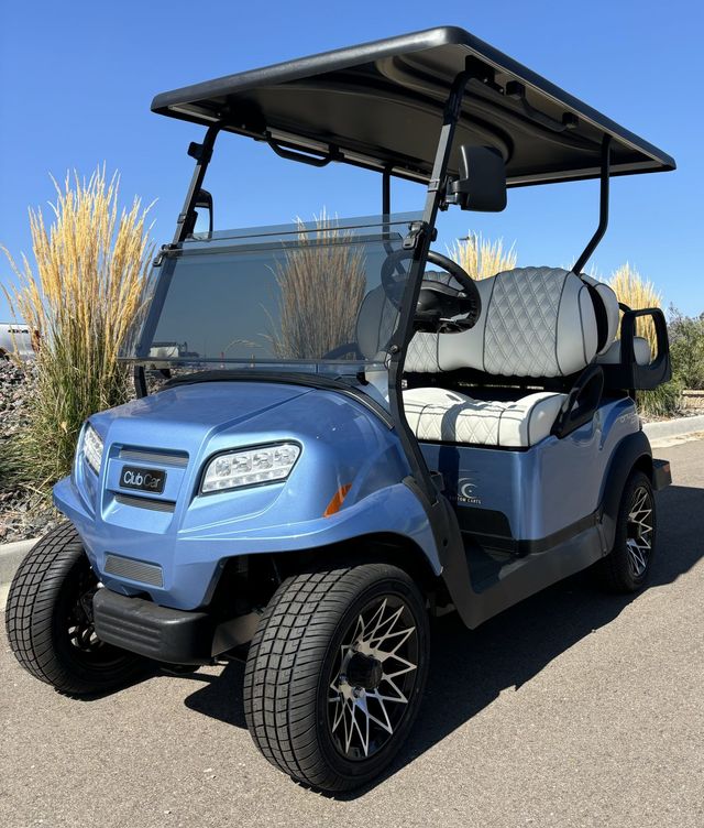 Blue golf cart with black roof and white seats parked outdoors on a sunny road.