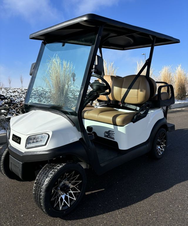 White and black golf cart with tan seats parked outdoors on a sunny day