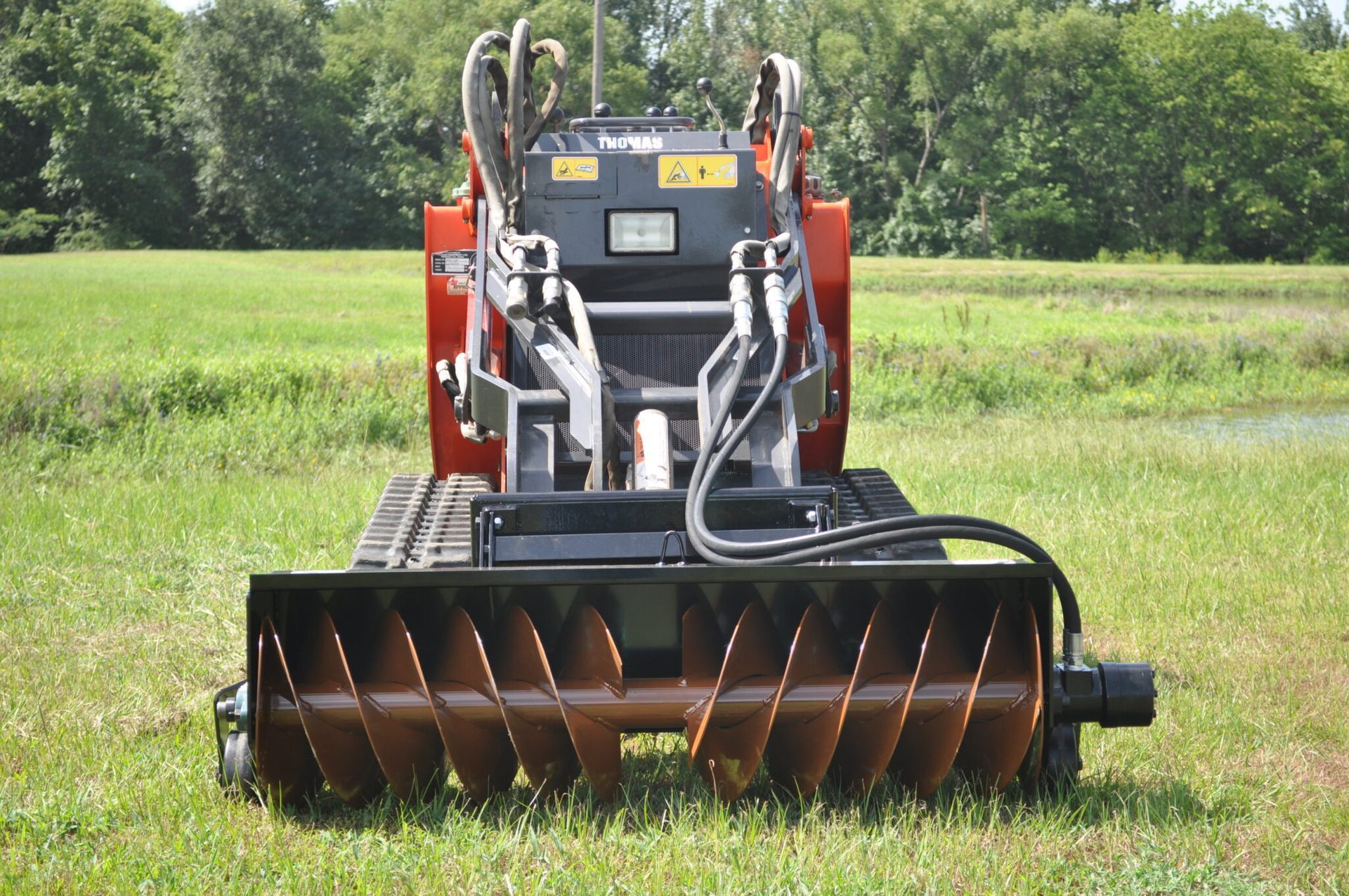 Orange and black mini-skid steer with mulching attachment on grassy field.